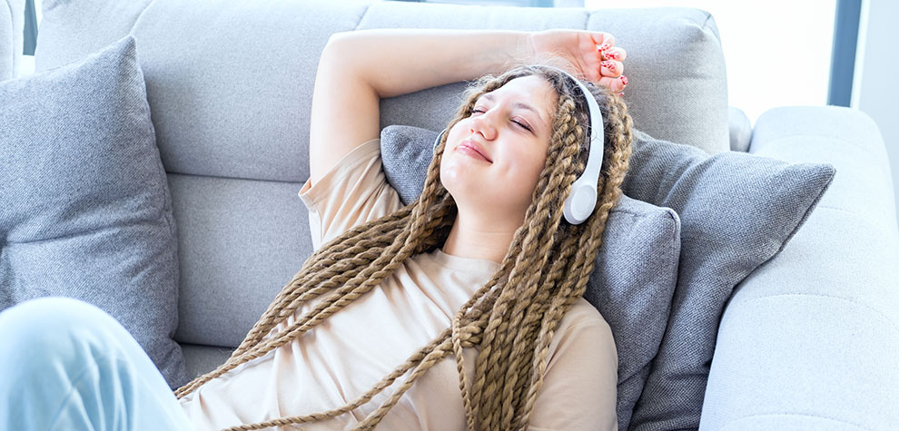 Happy female on her sofa with headphones on after buying weed online from the best online dispensary to order weed online. 