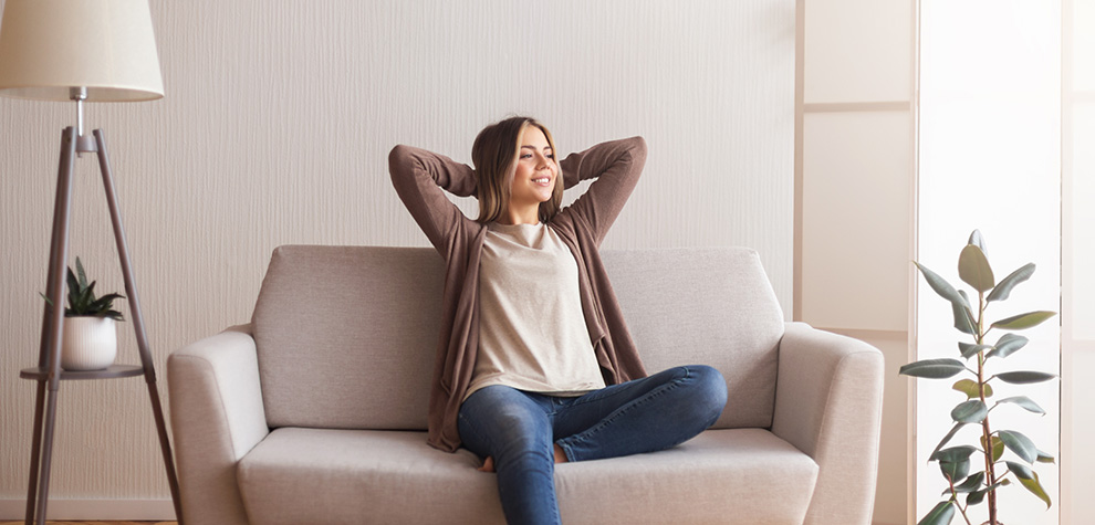 Smiling woman relaxing on her couch at home after micro dosing golden teacher mushrooms. Shrooms online Canada.