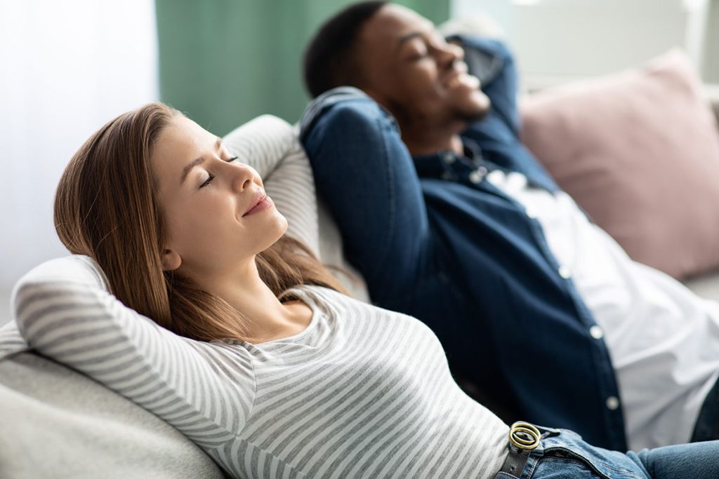 Couple relaxing on the sofa enjoying couch lock indica weed from MMJ Express online dispensary Canada.