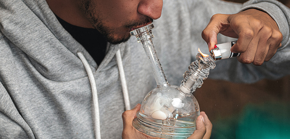 Man using a glass bong to smoke hash from an online dispensary and mail order weed store in Canada. Buy weed online.