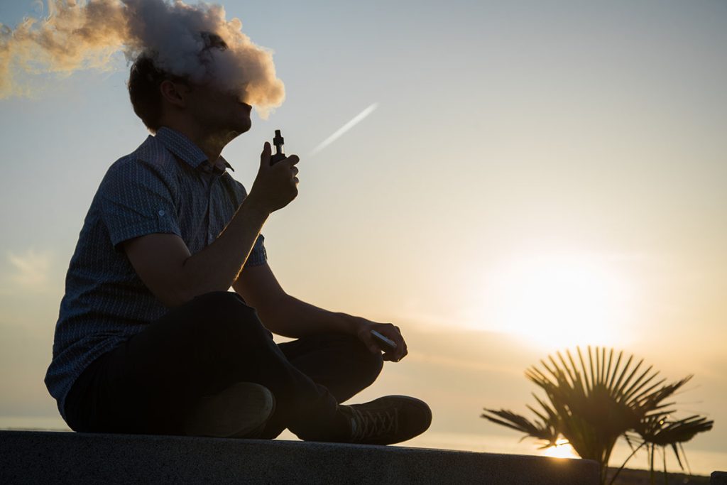 Man vaping weed with a dab pen outside at sunset after buying weed online from a mail order marijuana online dispensary in Canada.