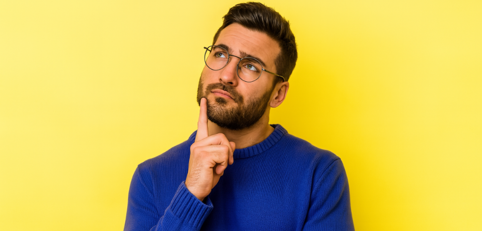 Thoughtful man in glasses and blue sweater pondering against yellow background, representing curiosity about hash resurgence in Canada
