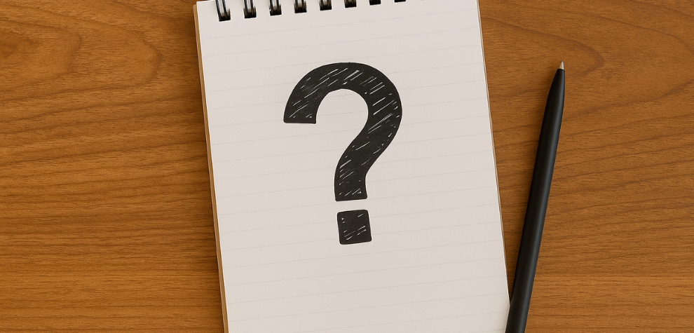 Notebook with a large black question mark drawn on a lined page, placed on a wooden desk with a black pen beside it