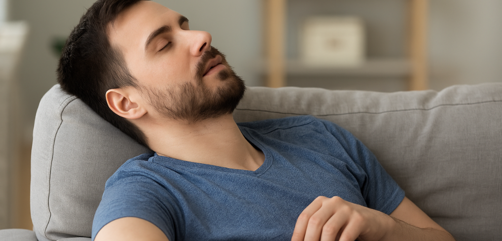 Man in a blue shirt relaxing and dozing off on a couch, illustrating MK Ultra weed’s strong sedative effects